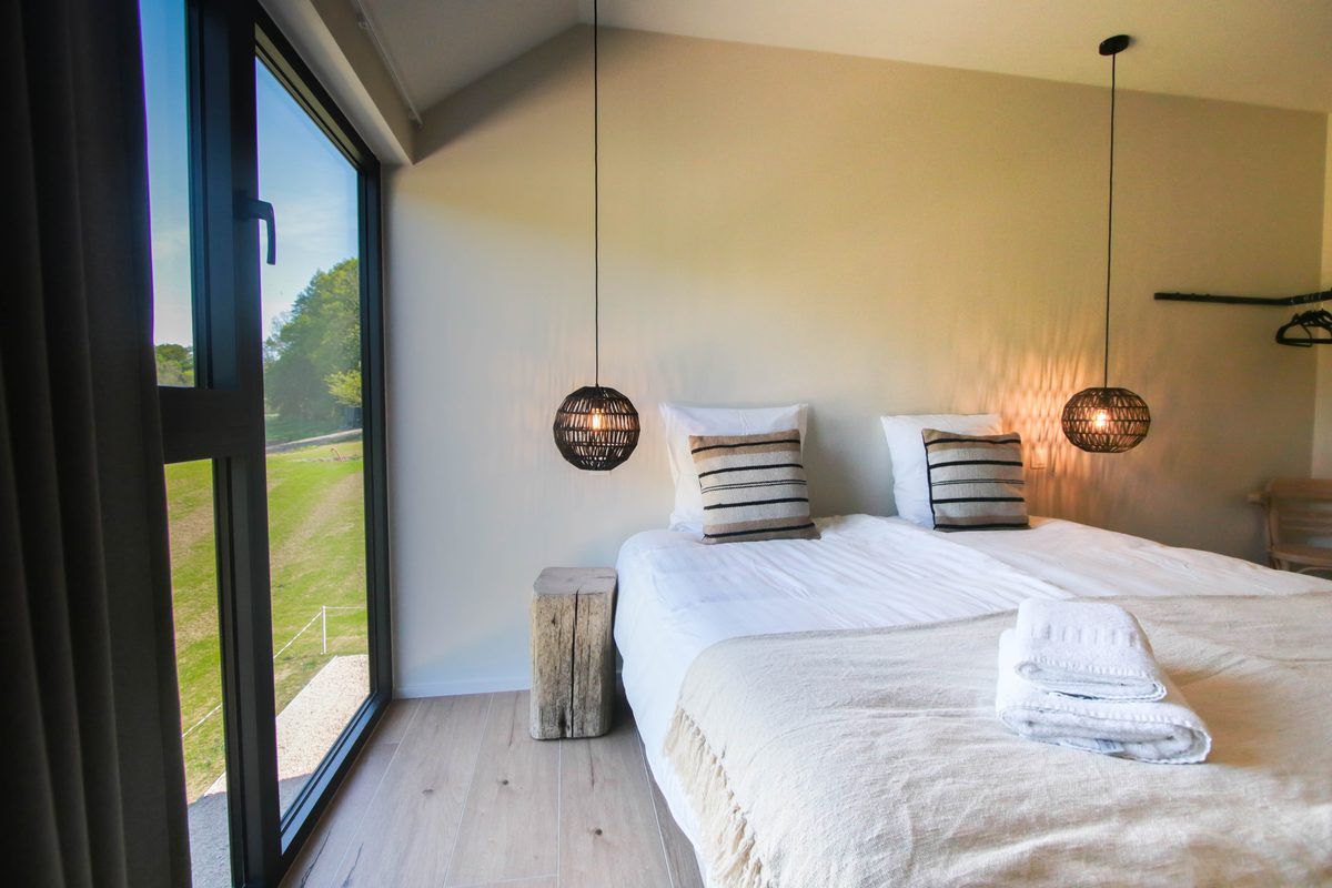 Chambre ouverte par une baie vitrée toute hauteur sur la prairie