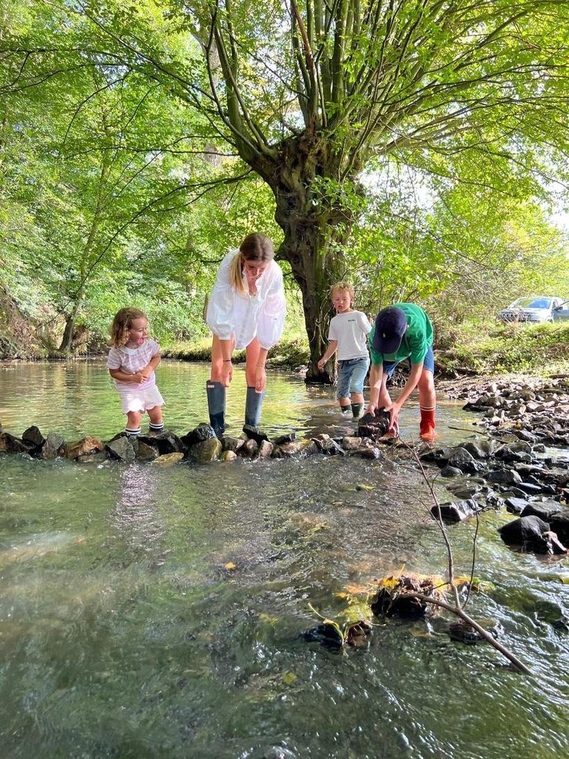 Une famille traverse la rivière sur les pierres, sous un saule